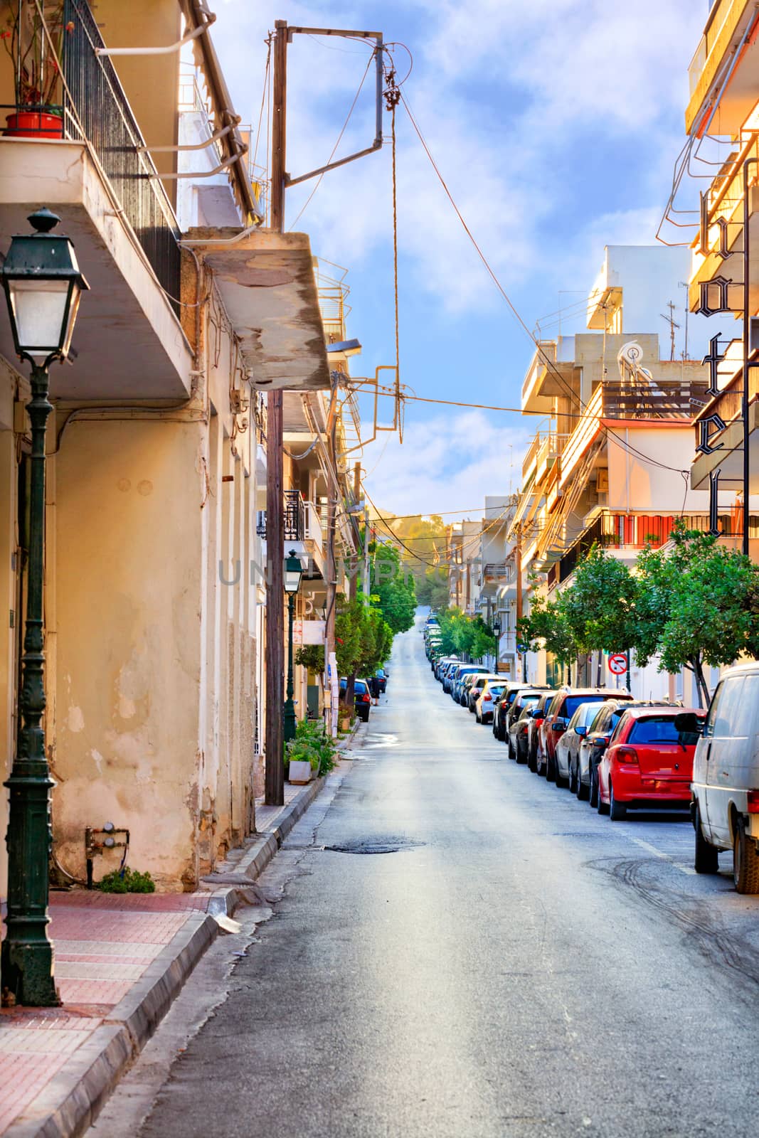 Deserted old narrow street of Loutraki in Greece in the early morning in the rays of the rising summer sun. by Sergii