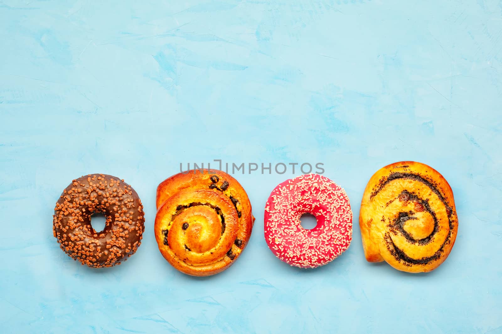 Delicious donuts with chocolate and strawberry icing and buns with poppy seeds and freshly baked raisins, close-up on a light turquoise surface. Pastry sweets for breakfast, image with copy space.