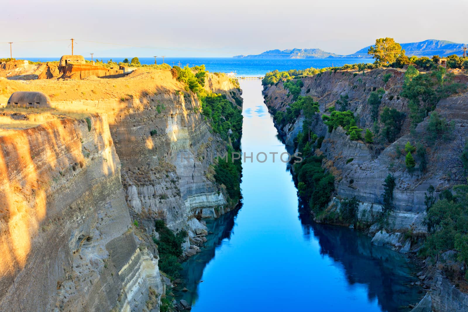 The Corinth Canal in the morning summer day illuminates the bright rising sun of Greece, a view of the Gulf of Corinth from the height, the channel connects the Saronicos of the Aegean Sea and the Corinthian Gulf of the Ionian Sea.