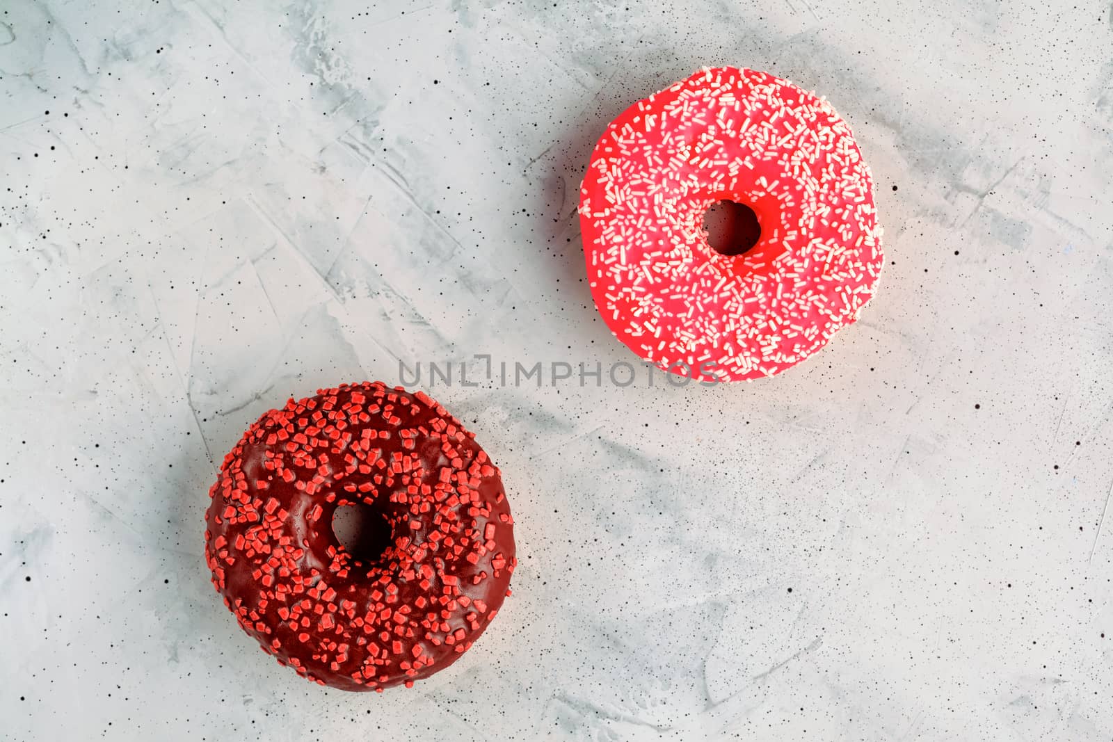 Two delicious donuts with chocolate and strawberry icing sprinkled on top with spicy crumbs closeup on a gray concrete surface. Confectionery sweets for breakfast, image with copy space.