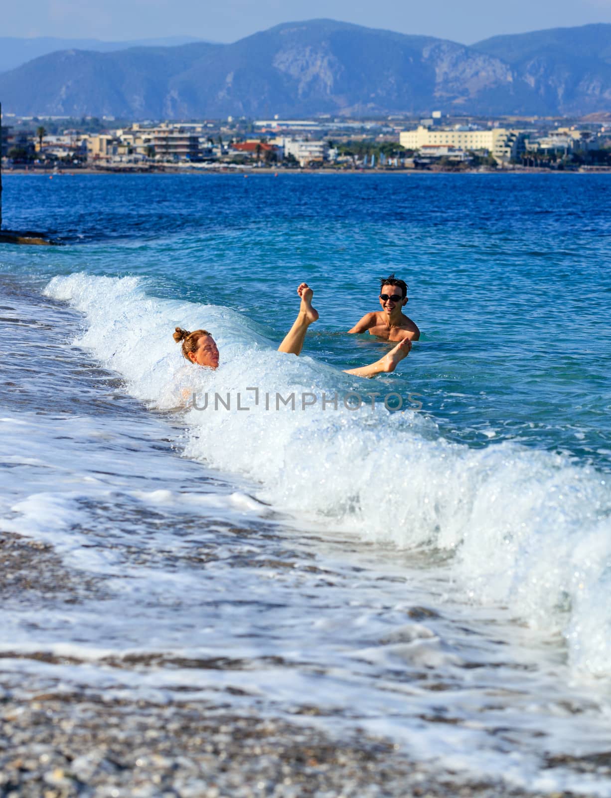 A coastal wave knocks down a young lady who enters the sea by a pebble beach. by Sergii