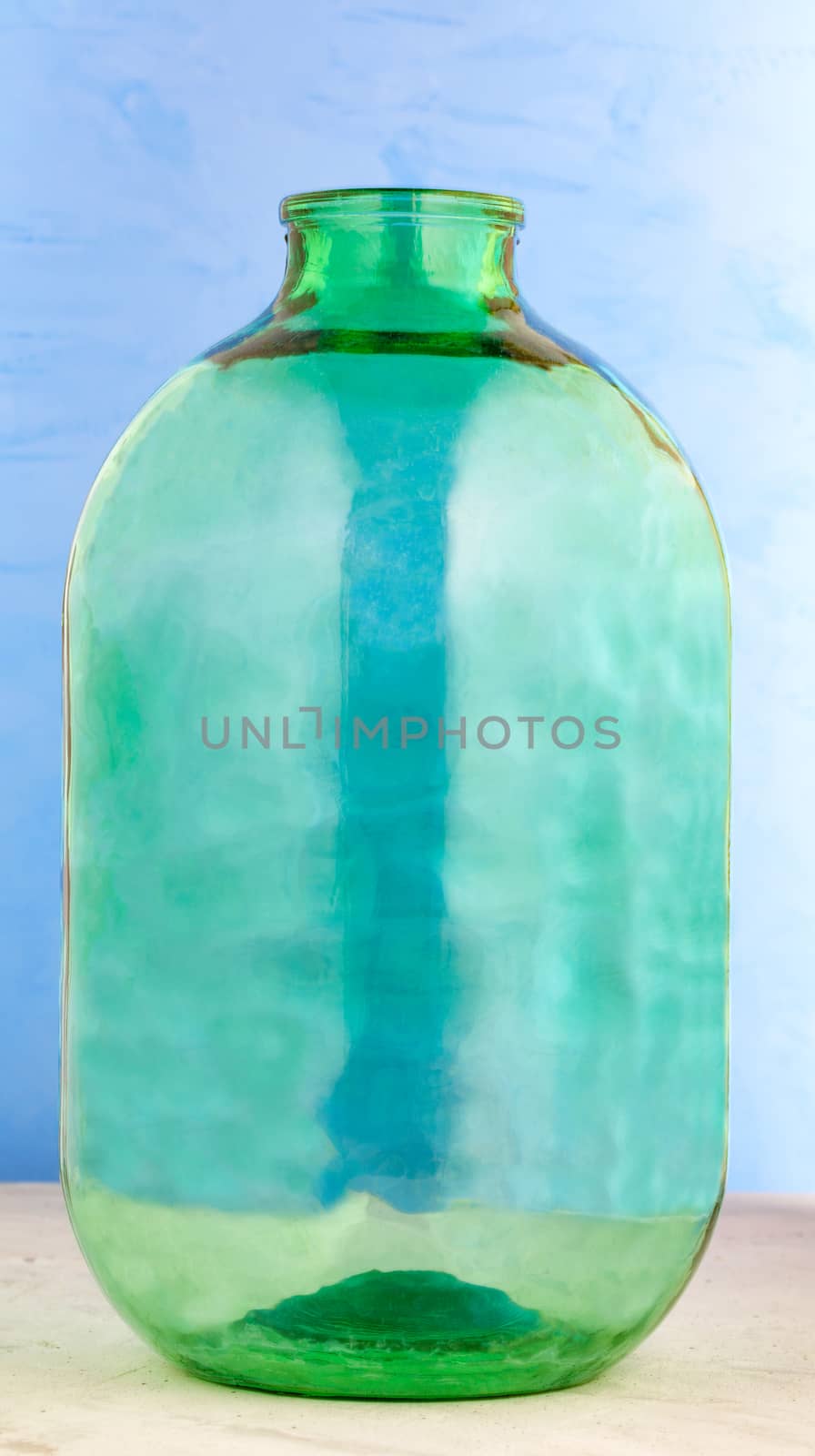 A 10 liter glass jar is made of thick green glass on a blue background. by Sergii