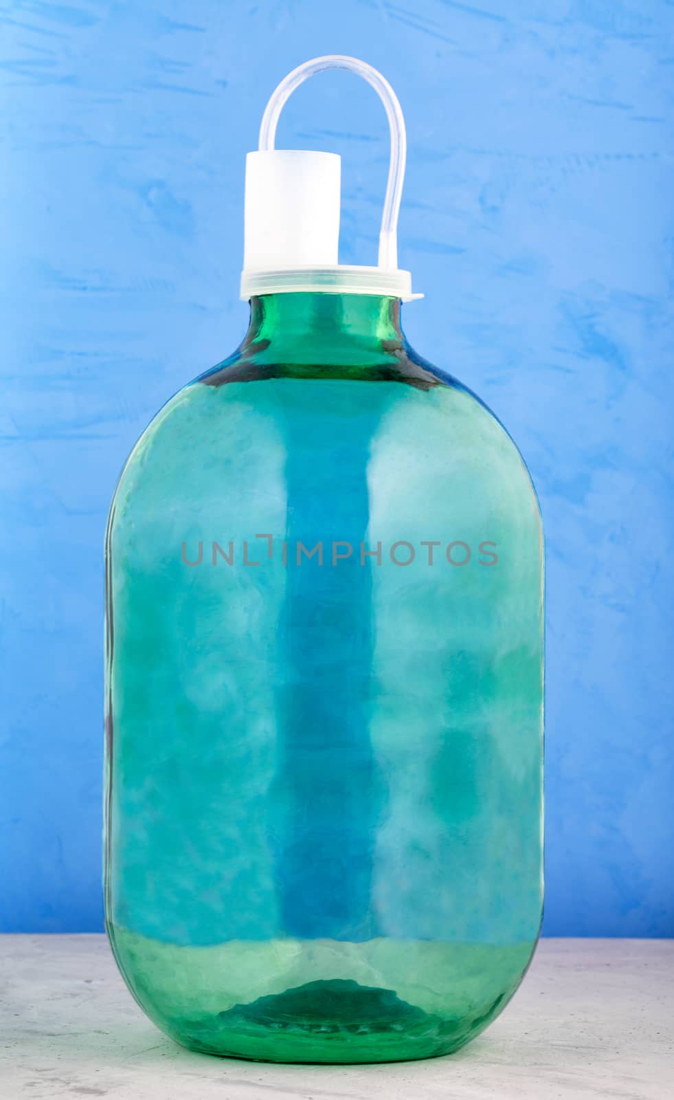 A 10 liter glass jar is made of thick green glass with a nylon cover with a water lock on a blue background. by Sergii