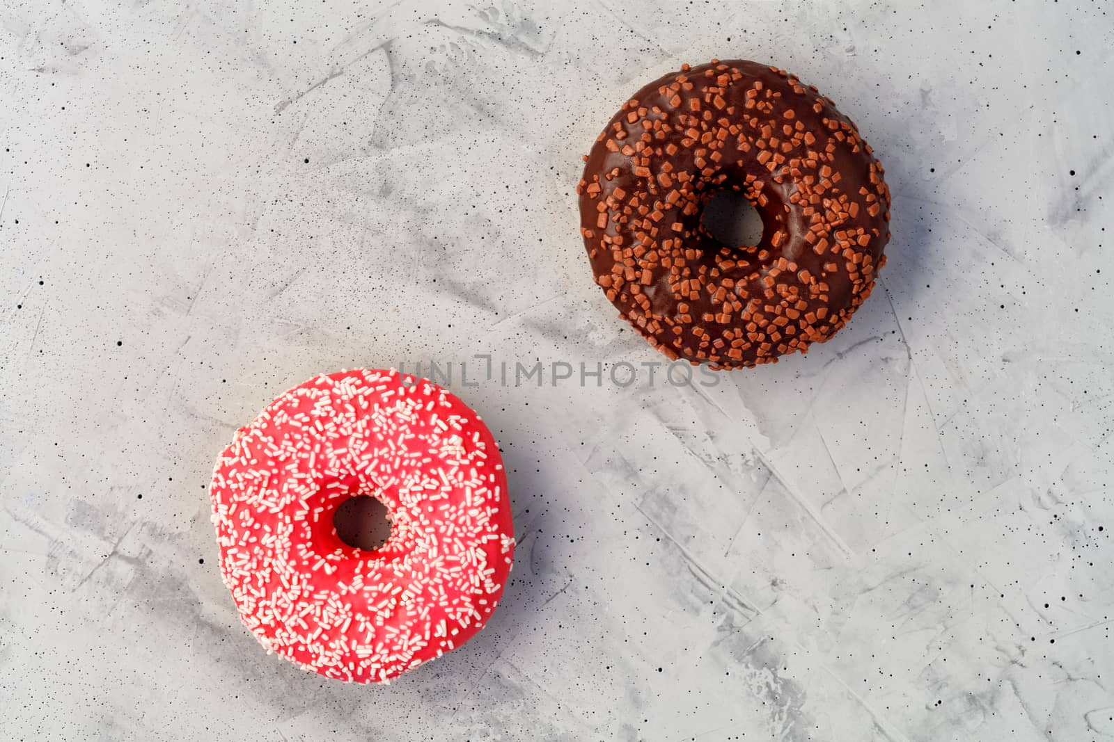 Two delicious donuts with chocolate and strawberry icing sprinkled with coconut and fruit chips on top, close-up on a gray concrete surface. Pastry sweets for breakfast, image with copy space.