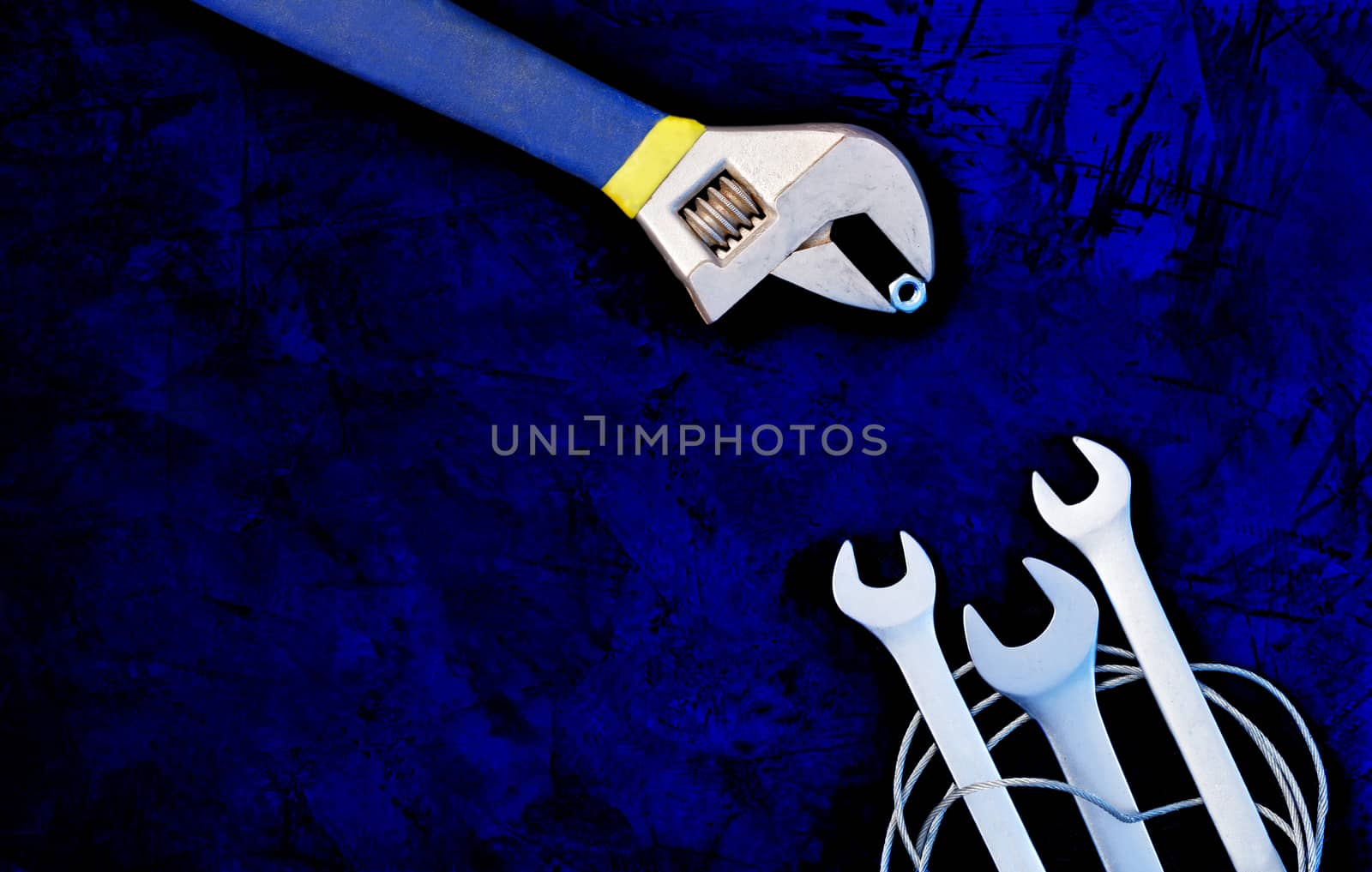 An old adjustable wrench teaches skill and provides food for new open-end wrenches, classic dark blue color background. The concept of communication and training, image with copy space.