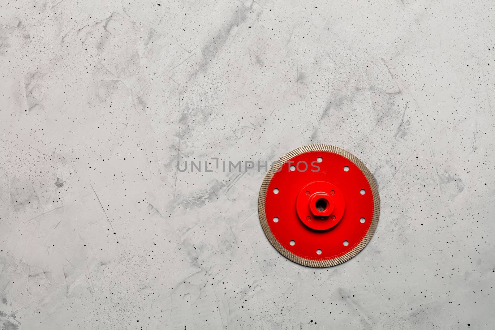 Cutting disc red color with diamond, a thin blade of diameter of 125 mm with a flange is used for precise cutting of the material against the background of gray concrete, image with copy space.