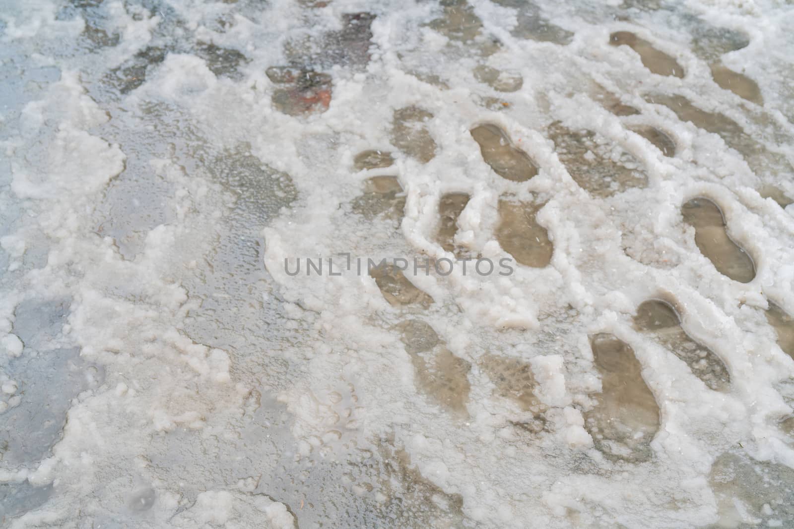 Traces of shoes in slush. The sidewalk is covered with melted snow.