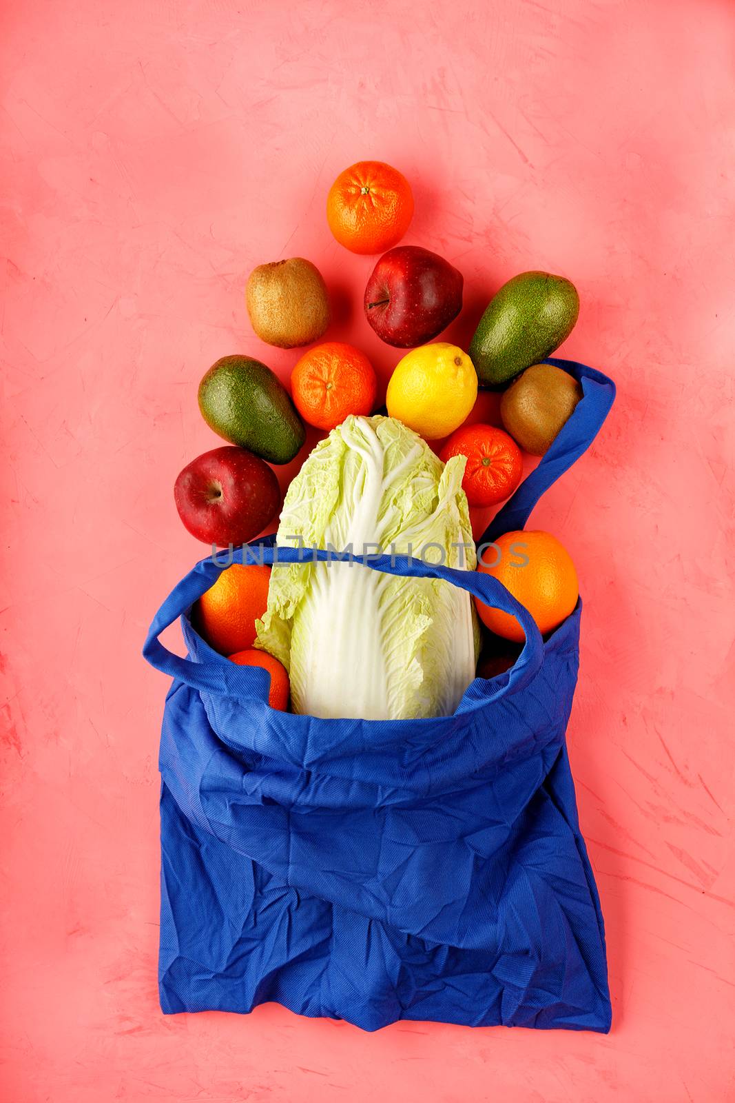 Eco-friendly cotton bag in classic blue color against a pink color background. Zero waste concept, plastic-free, eco-friendly shopping with fruits and vegetables, flat lay.