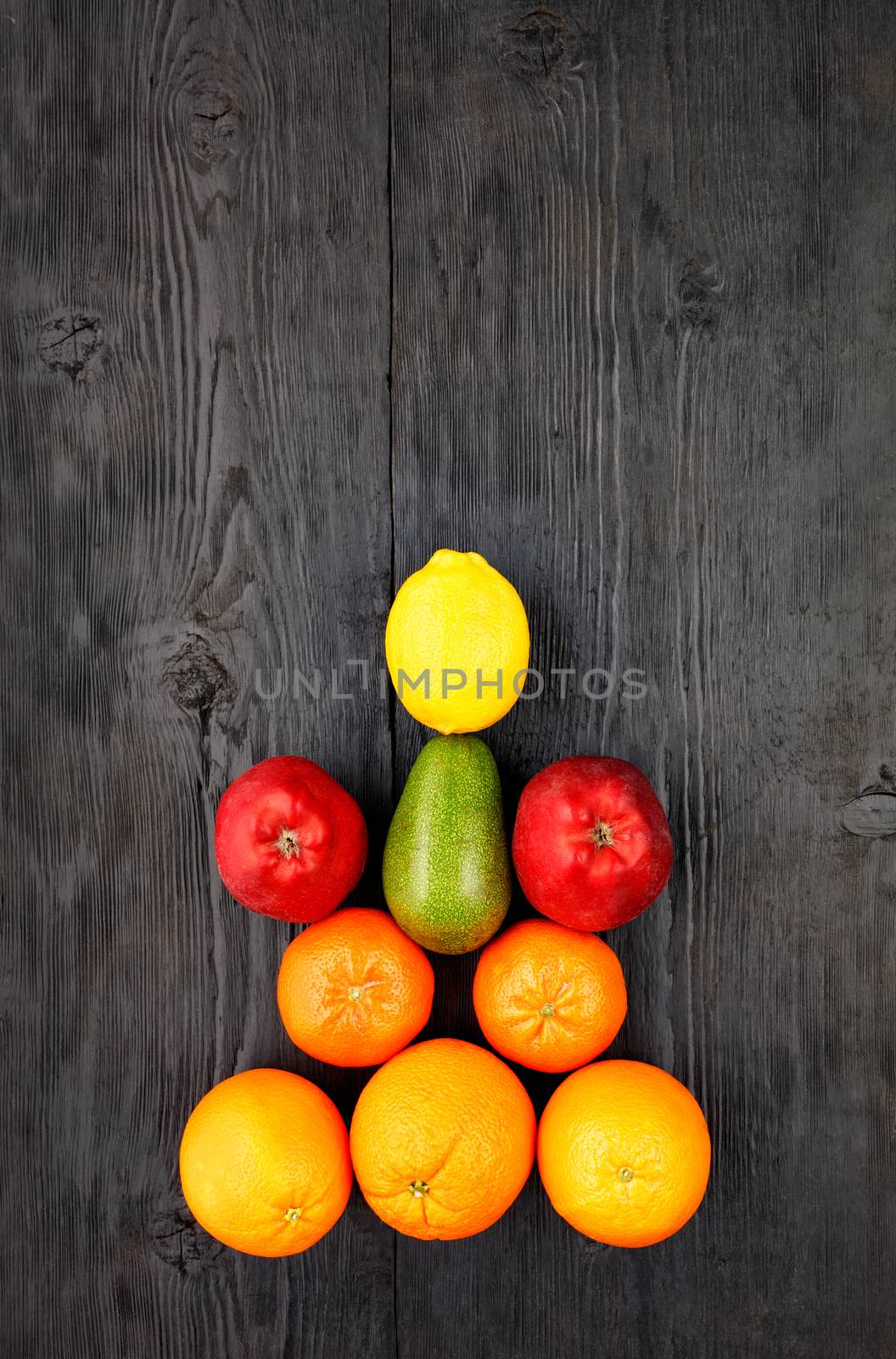 Ripe fruits and citrus fruits lie symmetrically on an old black wooden table. by Sergii
