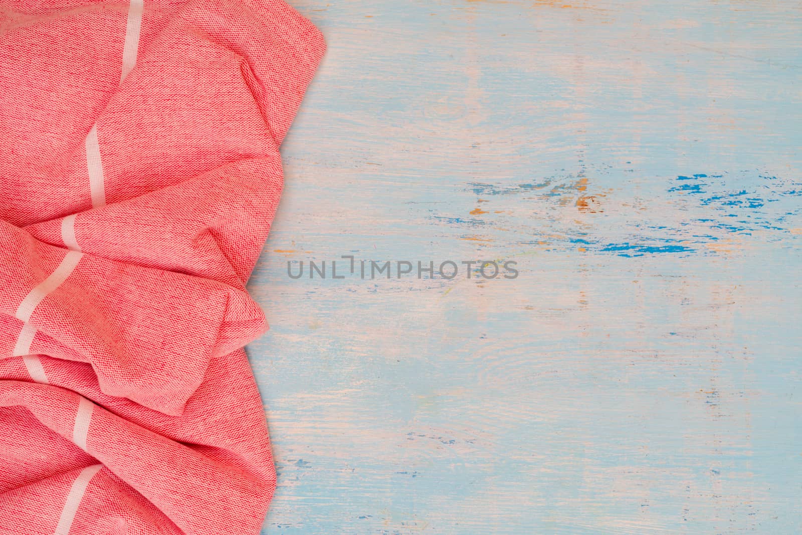 Red and white kitchen towel lies on wooden table. Texture of painted wood. Textured fabric folds.