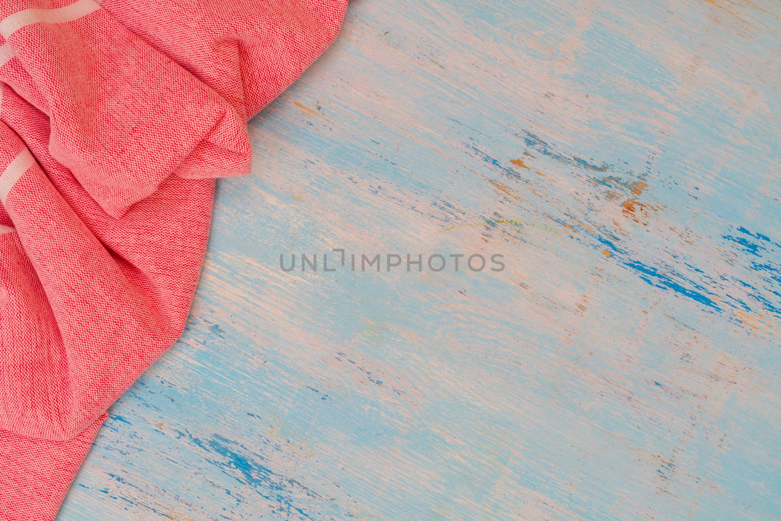 Red and white kitchen towel lies on wooden table. Texture of painted wood. Textured fabric folds.