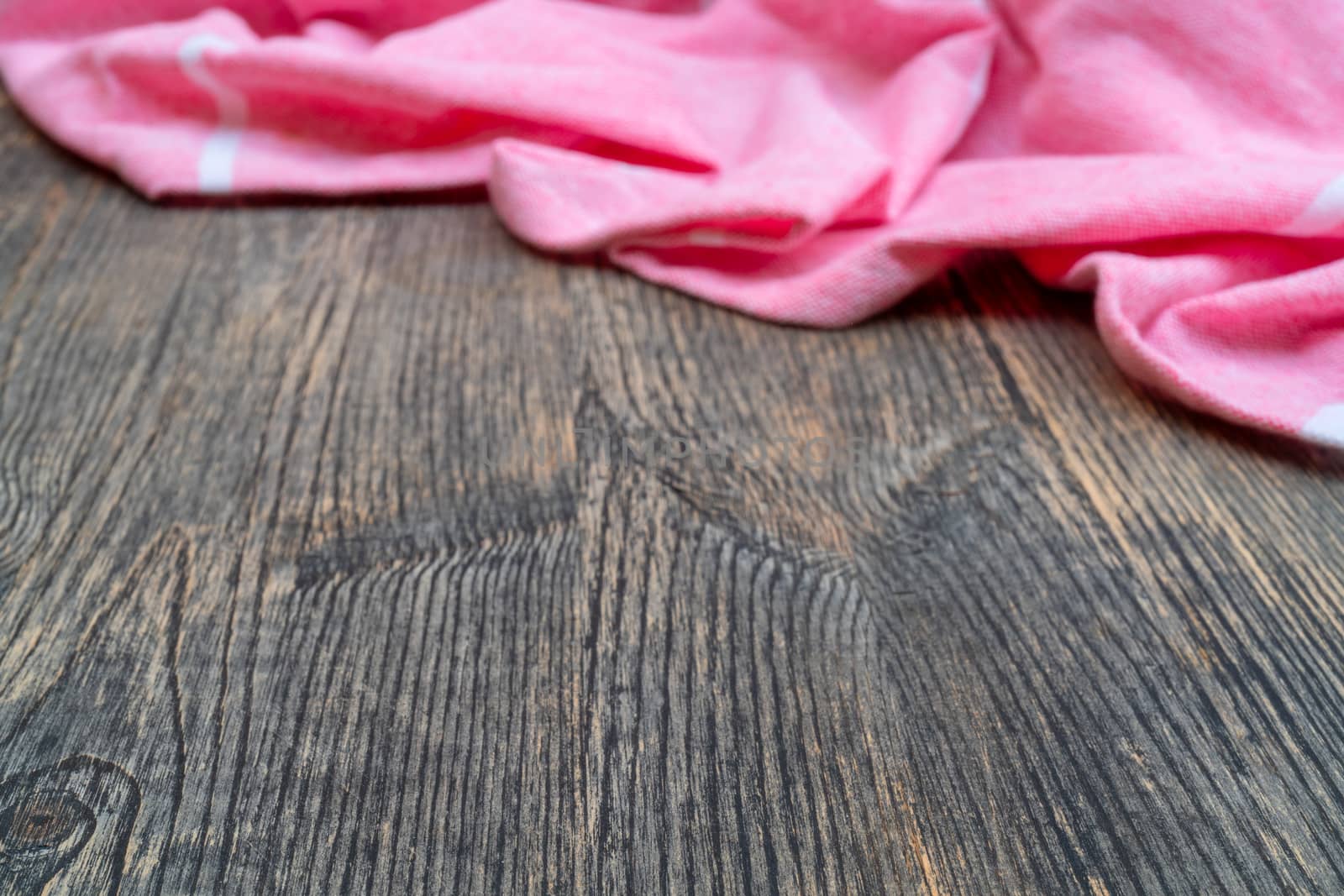 Red and white kitchen towel lies on wooden table. Texture of painted wood. Textured fabric folds.