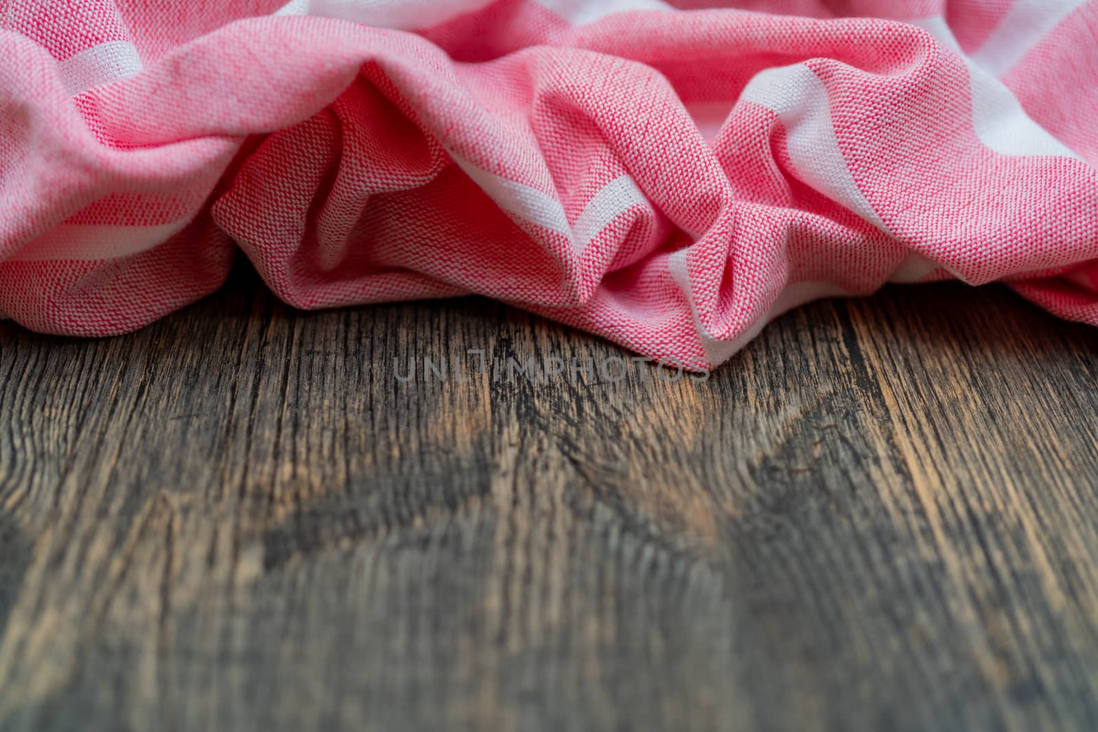 Red and white kitchen towel lies on wooden table. Texture of painted wood. Textured fabric folds.