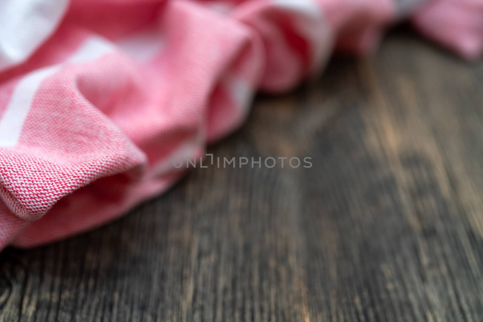 Red and white kitchen towel lies on wooden table. Texture of painted wood. Textured fabric folds.