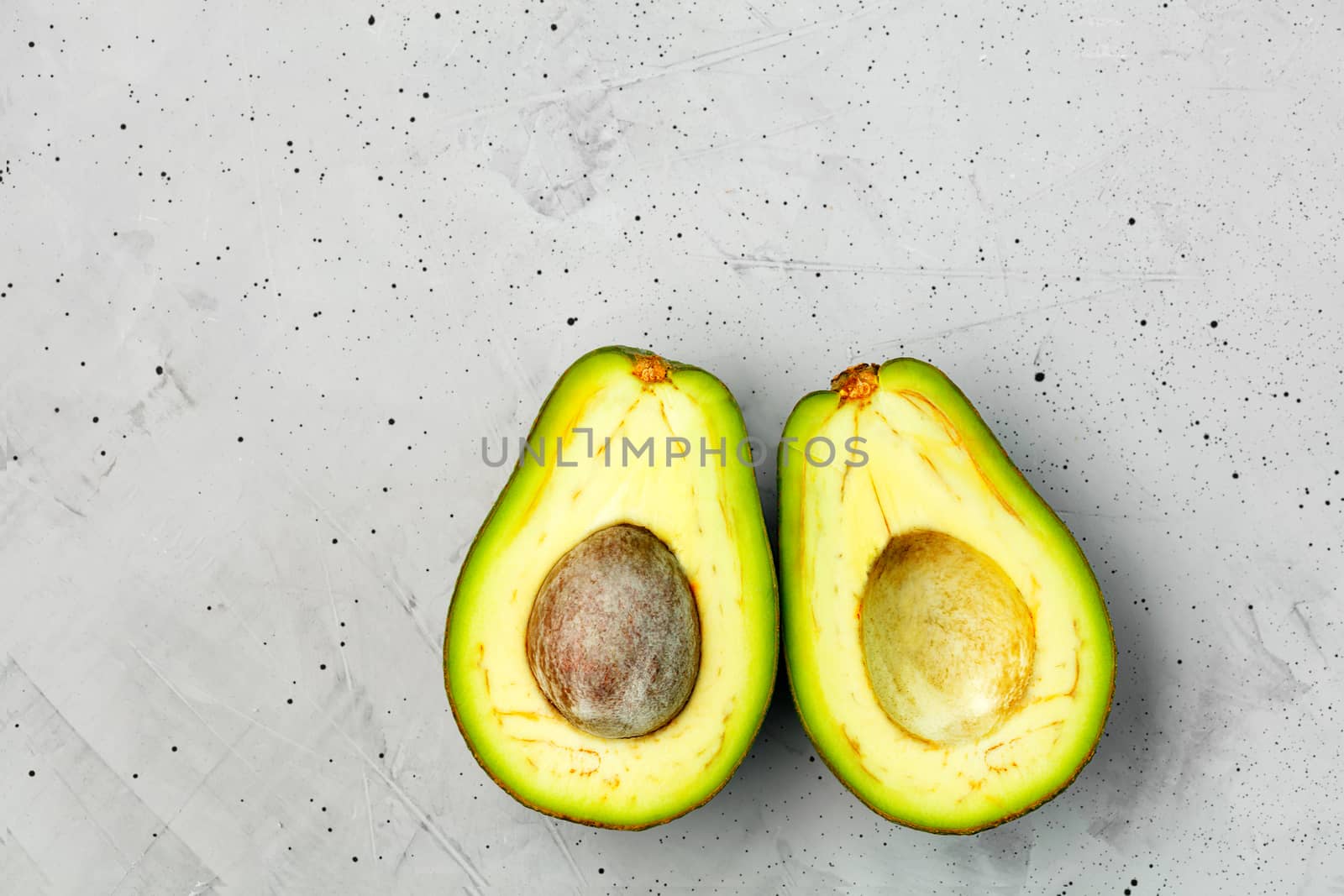 Avocado cut in half, one slice with core on gray concrete background, close-up. Delicious and nutritious fruit, image with copy space.