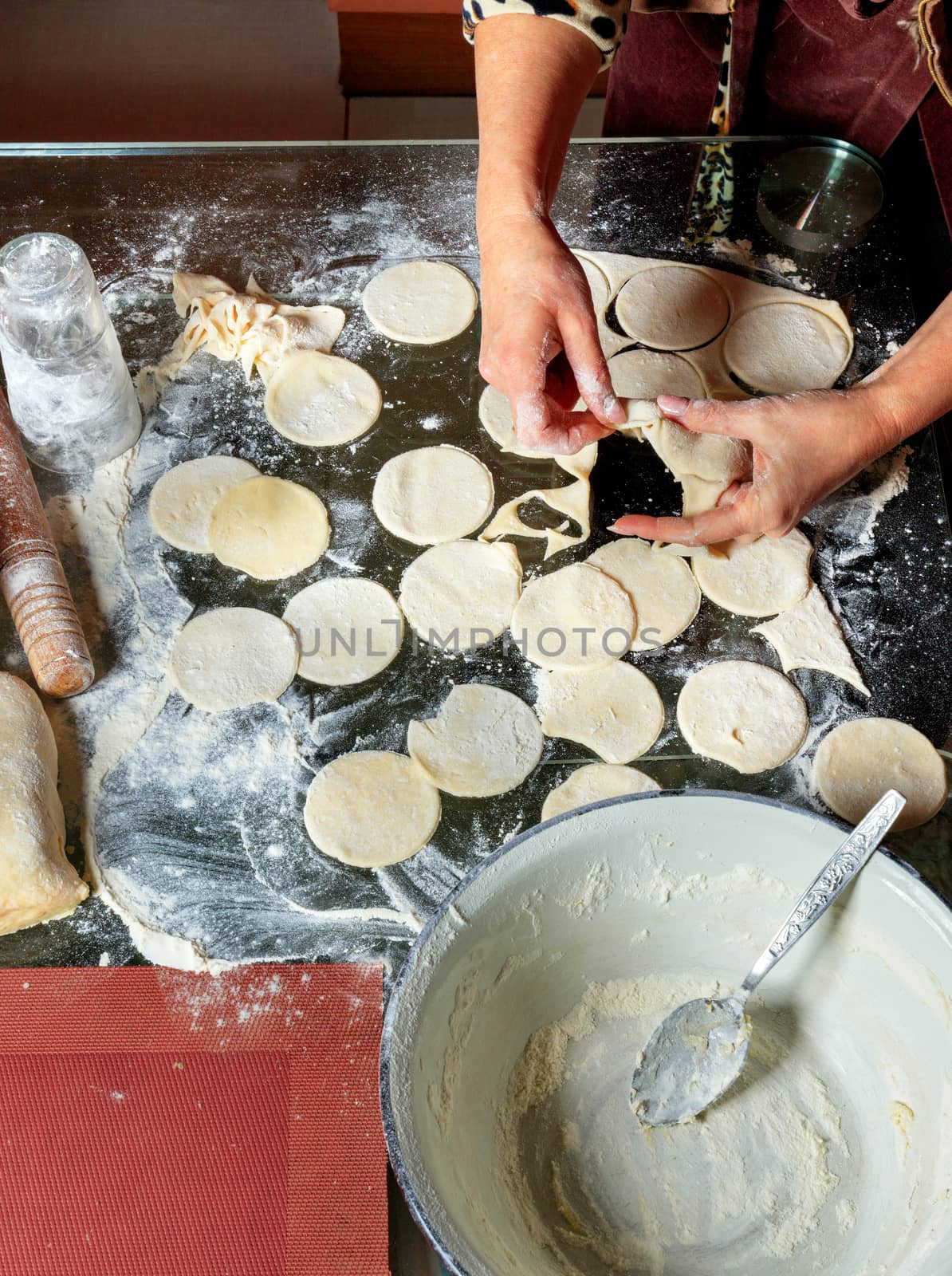 A woman using a rolling pin and a glass prepares round dough blanks for modeling dumplings in Ukrainian national cuisine.
