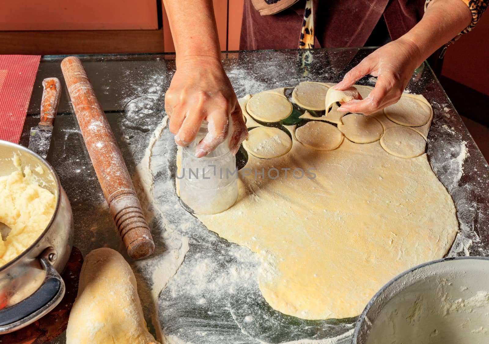 Housewife hands preparing round dough pieces for modeling dumplings in Ukrainian national cuisine.