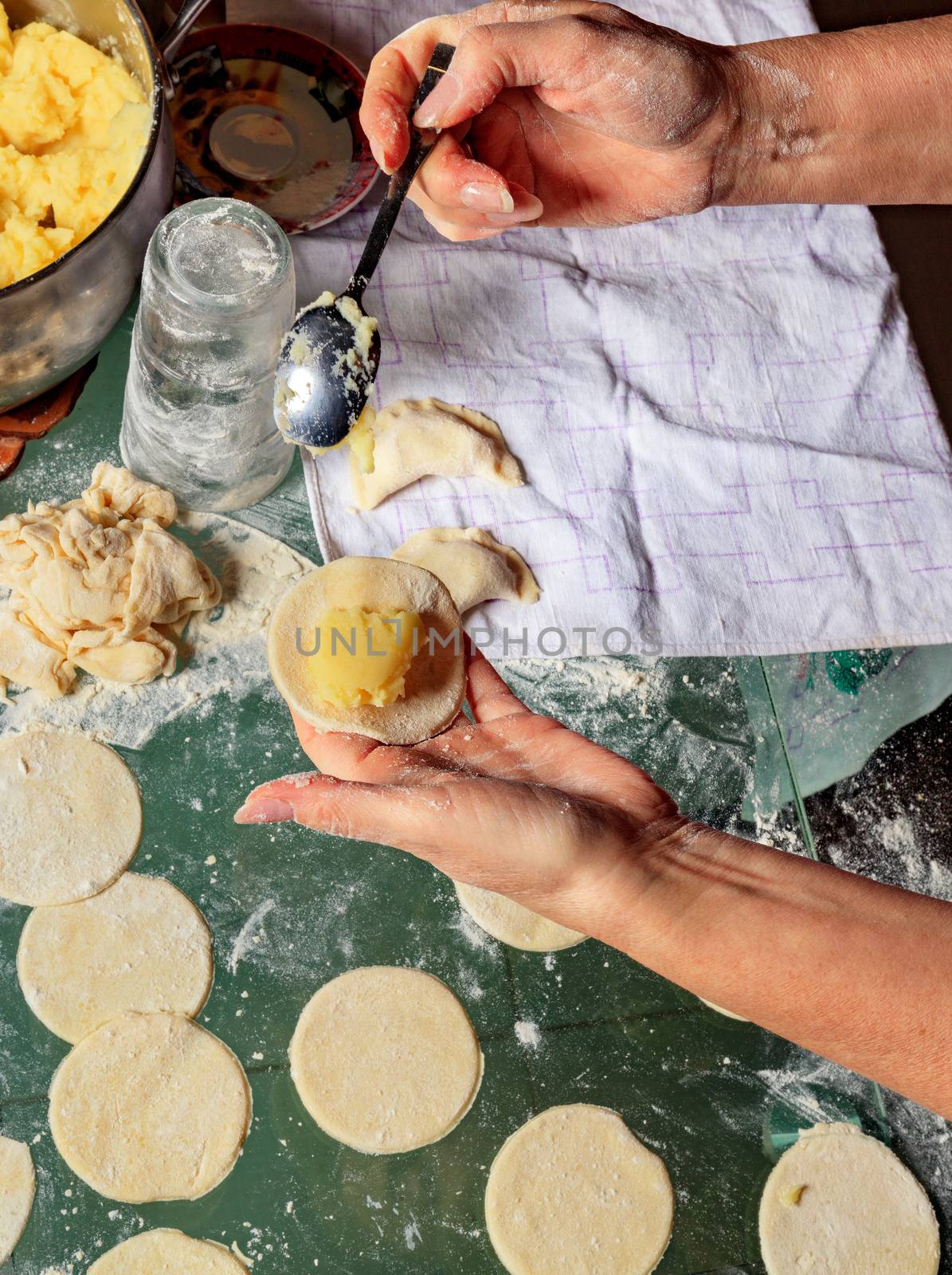 Woman using a spoon with her hands sculpts dumplings with potatoes in Ukrainian national cuisine, close-up.