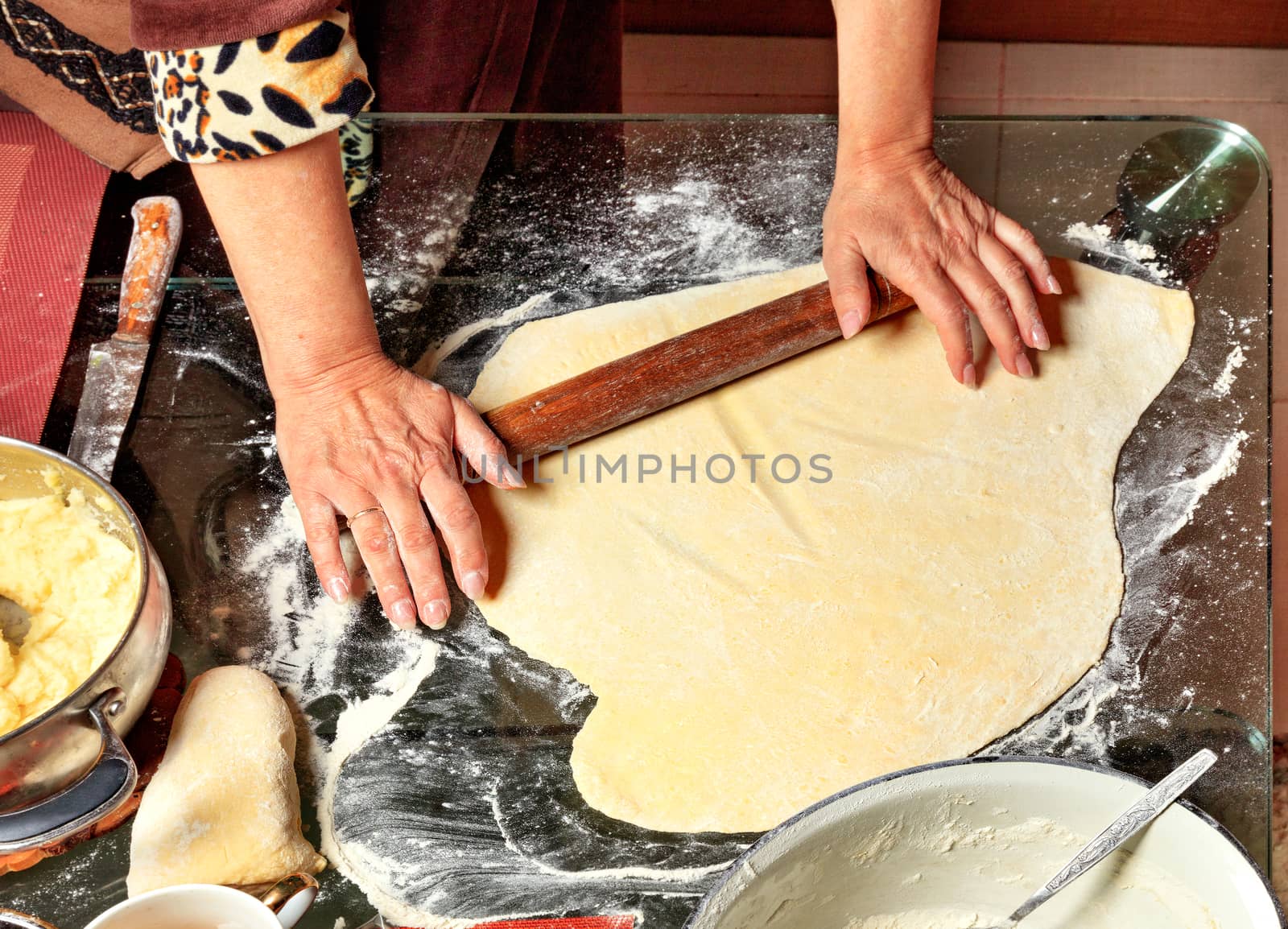 Housewife hands rolls the dough with a wooden rolling pin and prepares the ingredients for modeling dumplings in Ukrainian national cuisine.