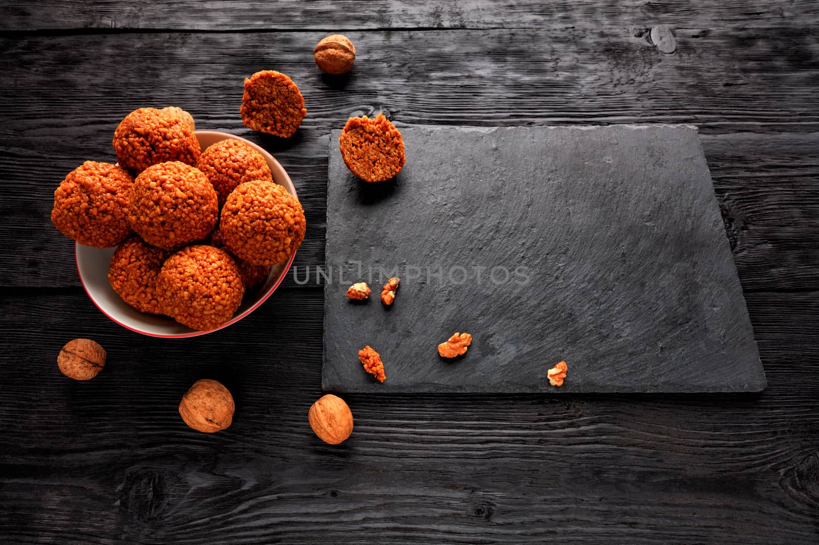 Homemade energy balls with walnuts, peanuts, honey and banana in a white porcelain plate on a black wooden background. Kitchen cutting board made of slate. Low key. View from above.