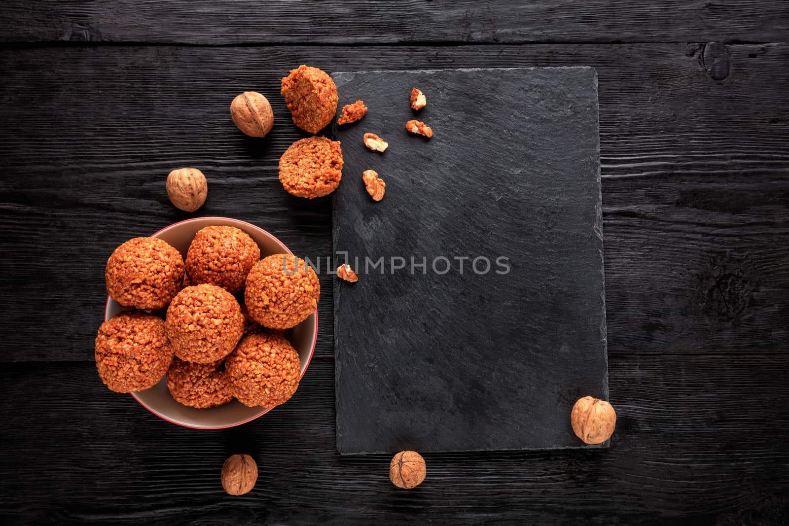 Homemade energy balls with walnuts, peanuts, honey and banana in a porcelain plate on a black wooden background,. Vegan vegetarian raw snacks. Healthy sweet food. Low key. Copy space flat lay, top view.
