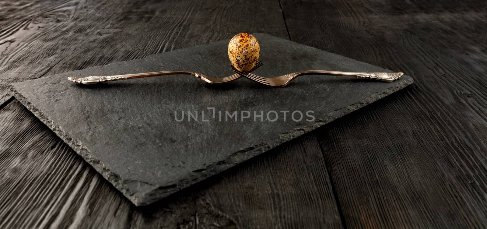 Quail egg on two old crossed forks on a kitchen cutting board. by Sergii
