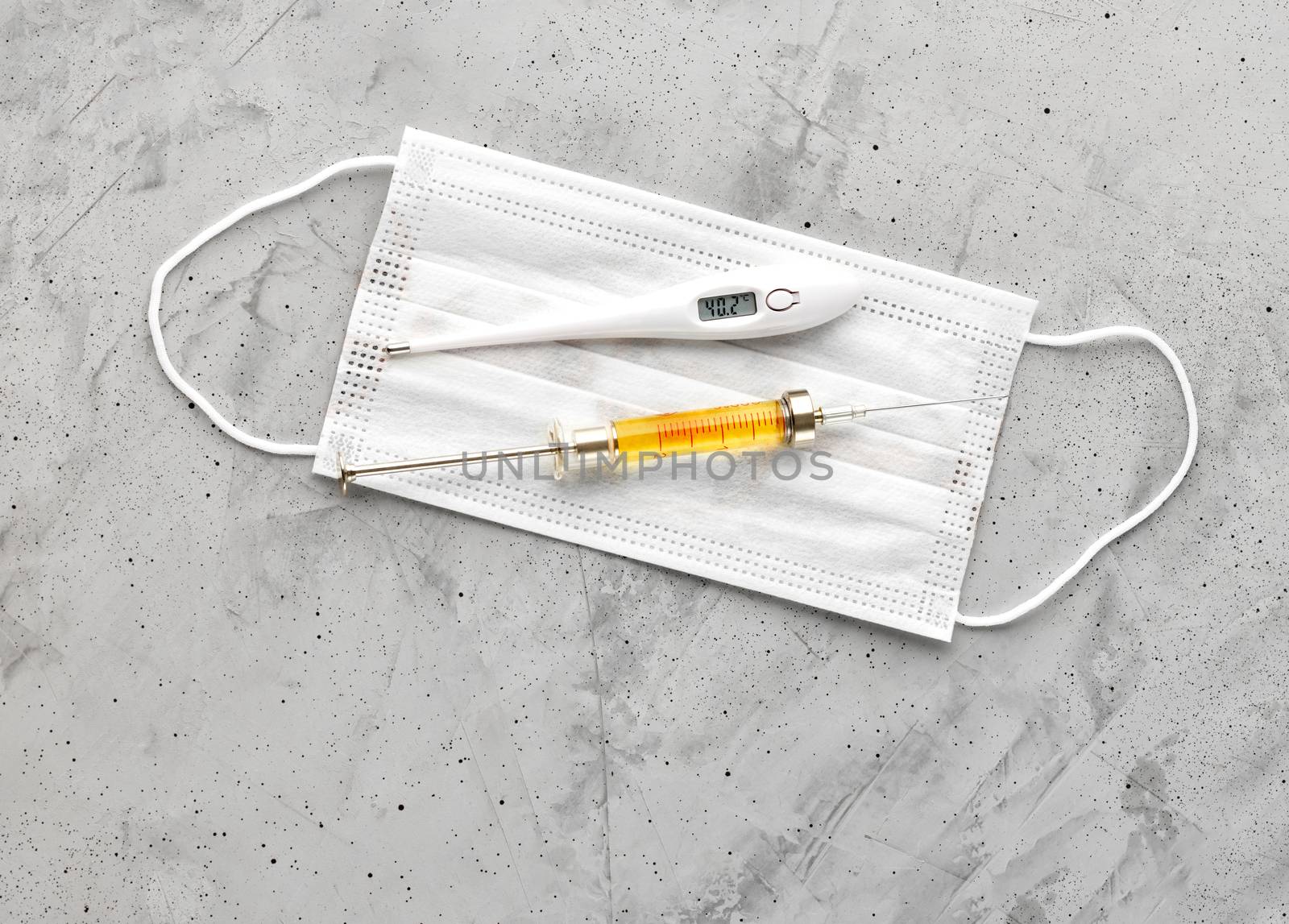 Medical mask, electronic thermometer and syringe with a yellow vaccine on a gray concrete background. The concept of protection against viruses, influenza and high body temperature. Copy space flat lay, top view.