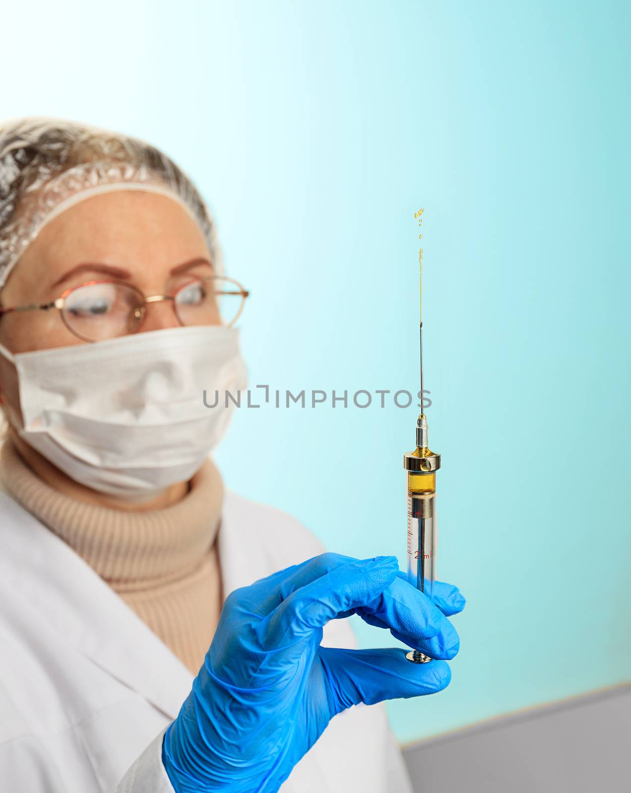 Virus protection concept. Medical theme on a light turquoise background. A small injection syringe in the doctor s hand in a latex medical glove and a face mask that checks the patency of the vaccine.