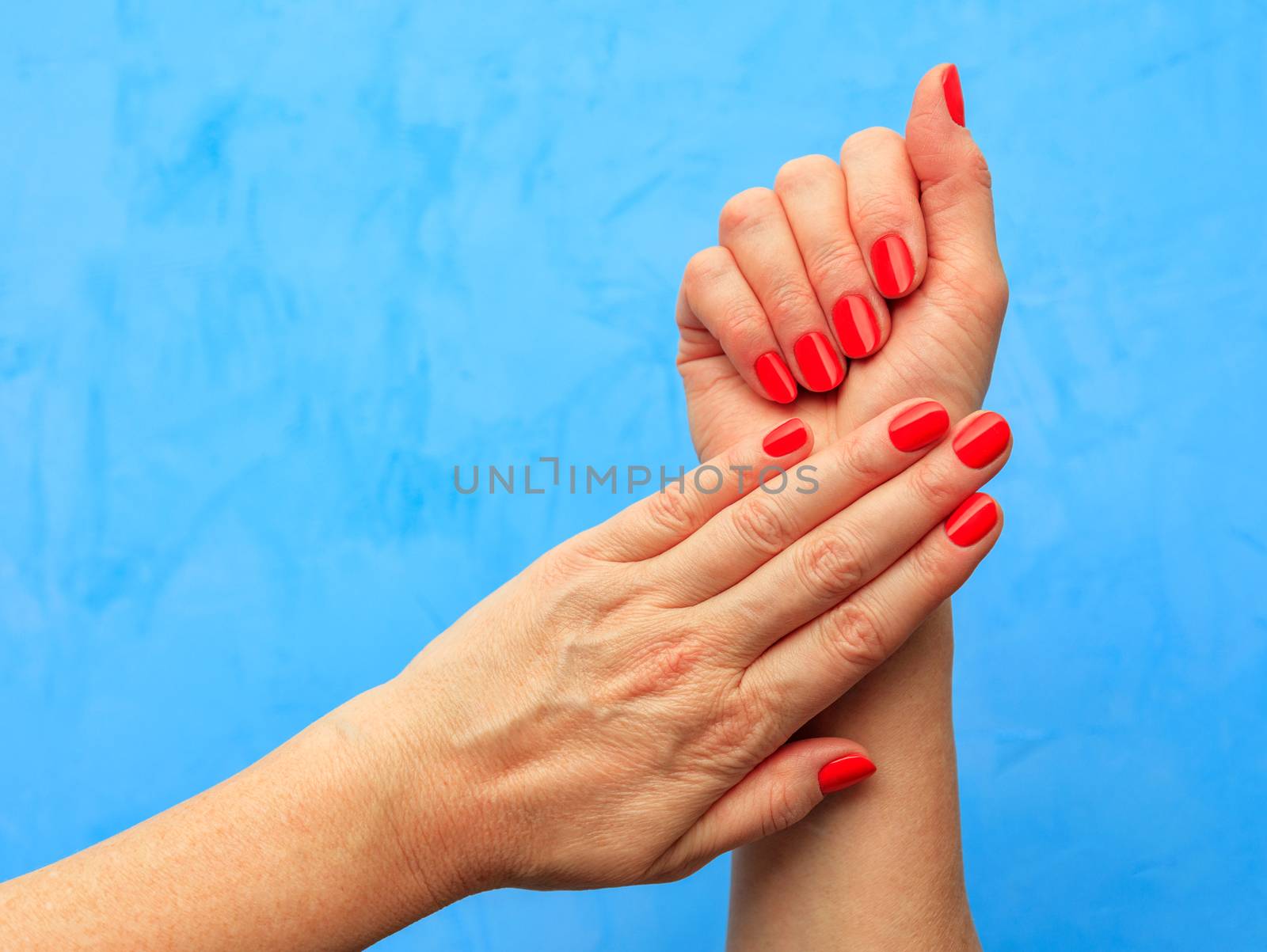 Beautiful female nails with beautiful Italian manicure Solferino blood red color on a turquoise background.