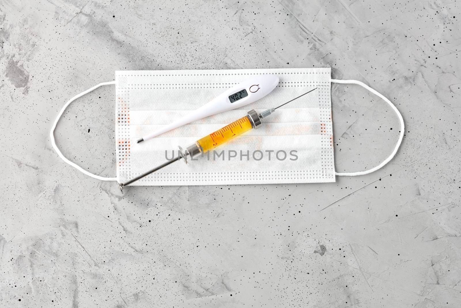 Medical mask, electronic thermometer and syringe with a yellow vaccine on a gray concrete background. The concept of protection against viruses, influenza and colds. Copy space, top view.