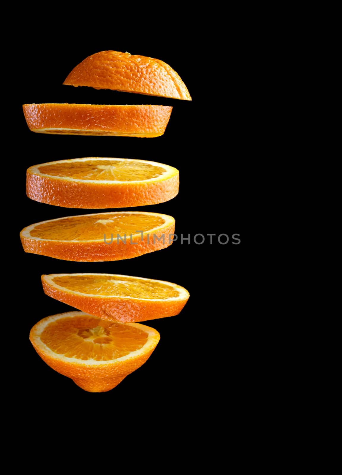 Flying chopped orange on a black background. Copy space, verticalal image.