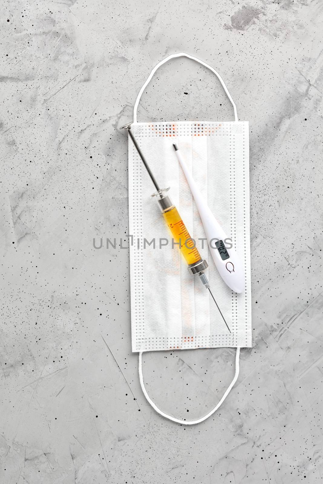 Medical mask, electronic thermometer and syringe with a yellow vaccine on a gray concrete background. The concept of protection against viruses, influenza and colds. Copy space, vertical image.