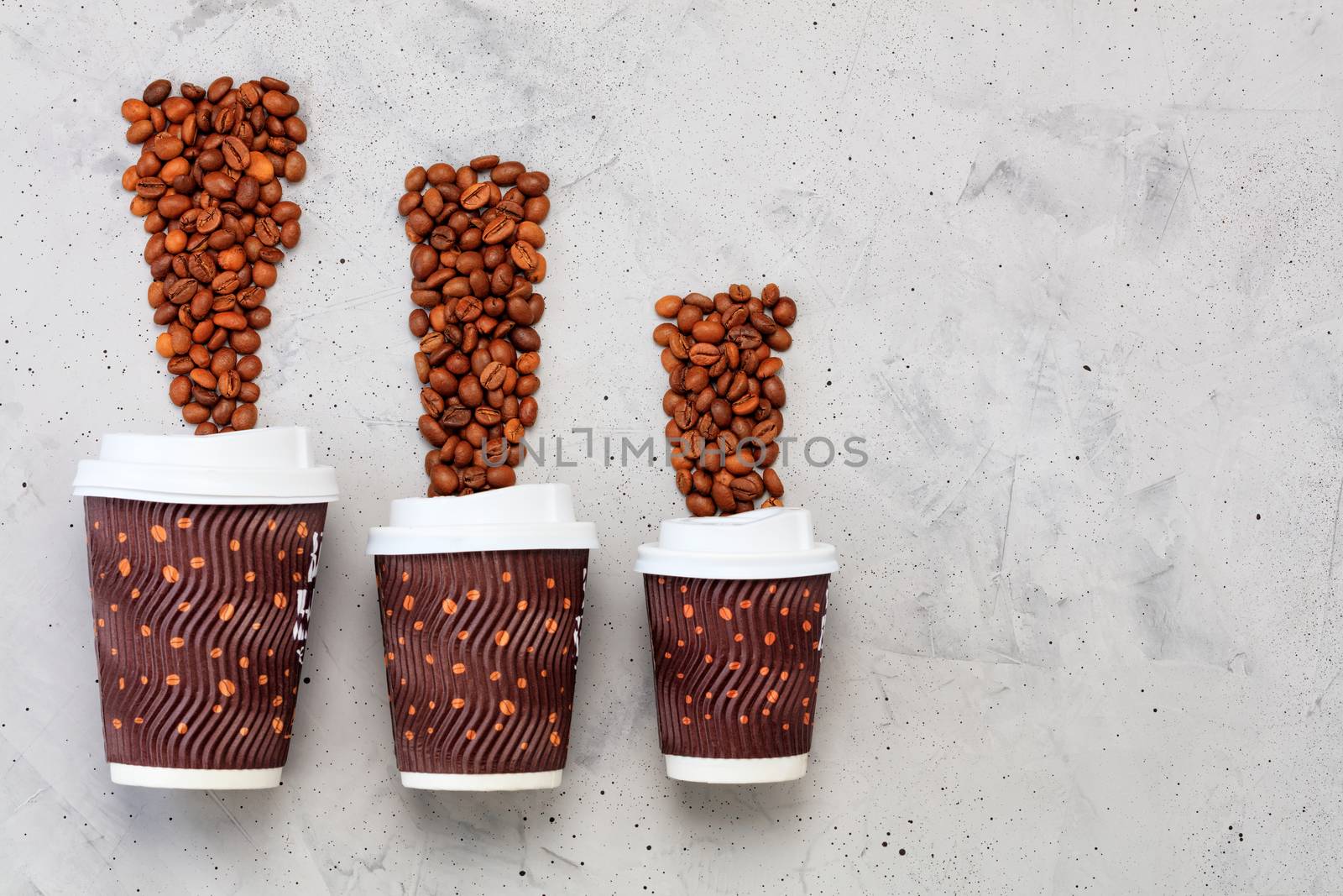 Coffee beans and three disposable cardboard mugs of different capacities for hot drinks, with a lid on a gray concrete background.