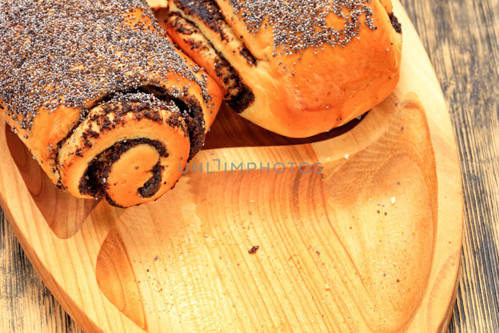 Ruddy fresh rolls with poppy seeds lies on wooden tray on wooden surface closeup, copy space.