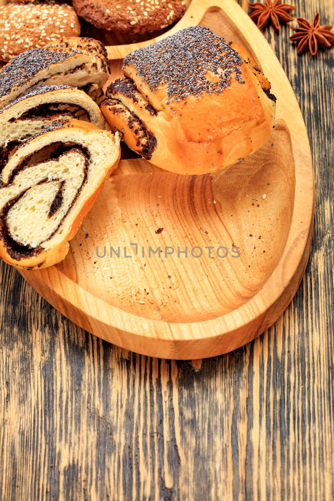 Sliced ruddy fresh bun with poppy seeds and cookies lie on a wooden cutting board on a wooden surface close-up by Sergii