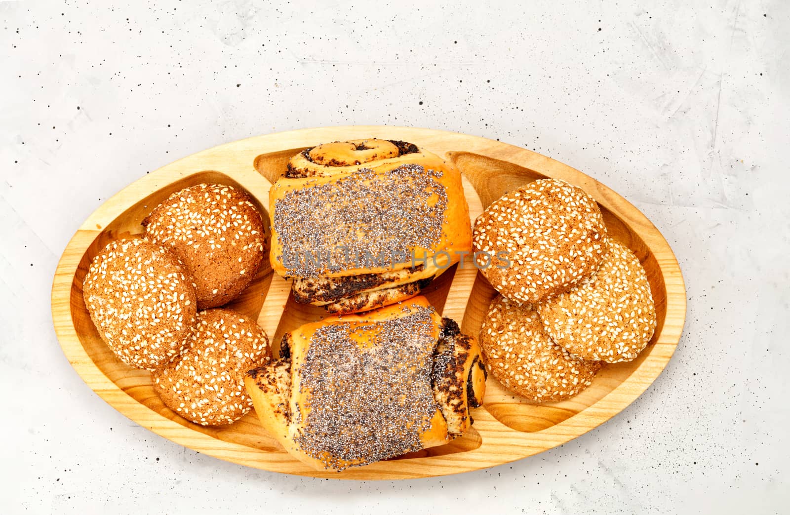Fresh buns with poppy seeds and cookies with sesame seeds on a wooden surface, on a background of gray concrete, close-up, copy space.