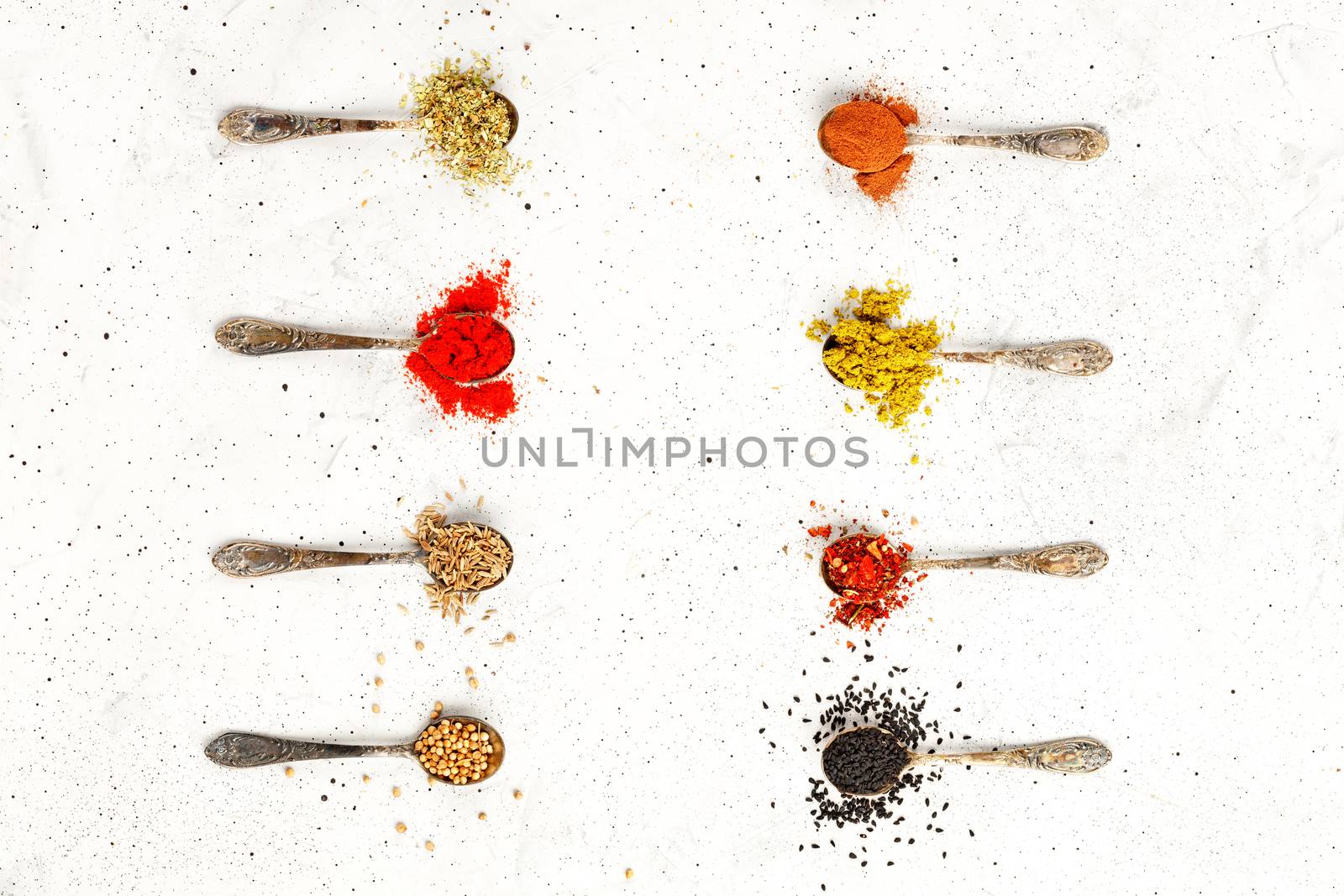 Old silver spoons with various asian spices mayran, caraway, cinnamon, hops, zira, allspice, ground paprika, corinade on a gray concrete background. Top view,, copy space.