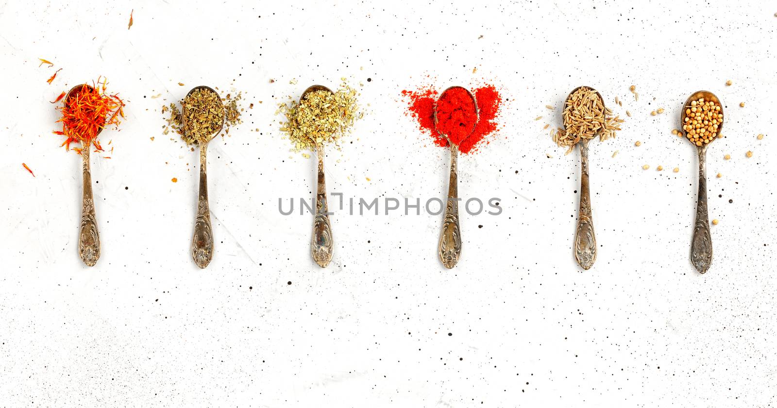 Old silver spoons with various asian spices saffron, zira, corinade, ground paprika, mayran, oregano on a gray concrete background.