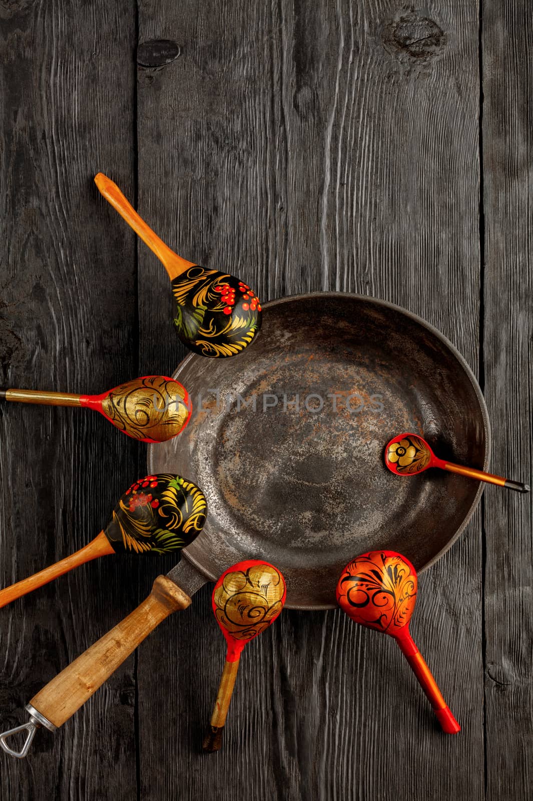 Vintage cast iron skillet and wooden old painted spoons on black rustic wood background. Tableware with copy space, flat lay, top view.