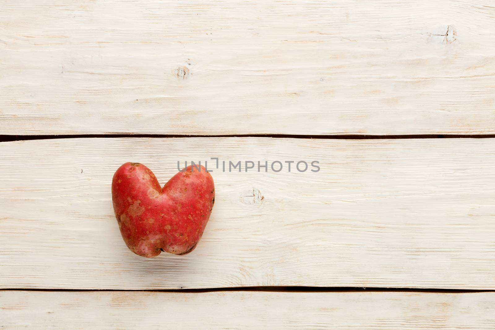 Ugly funny vegetables, heart-shaped potatoes on a white wooden background. The concept of grungy vegetables or food waste. Top view, copy space.