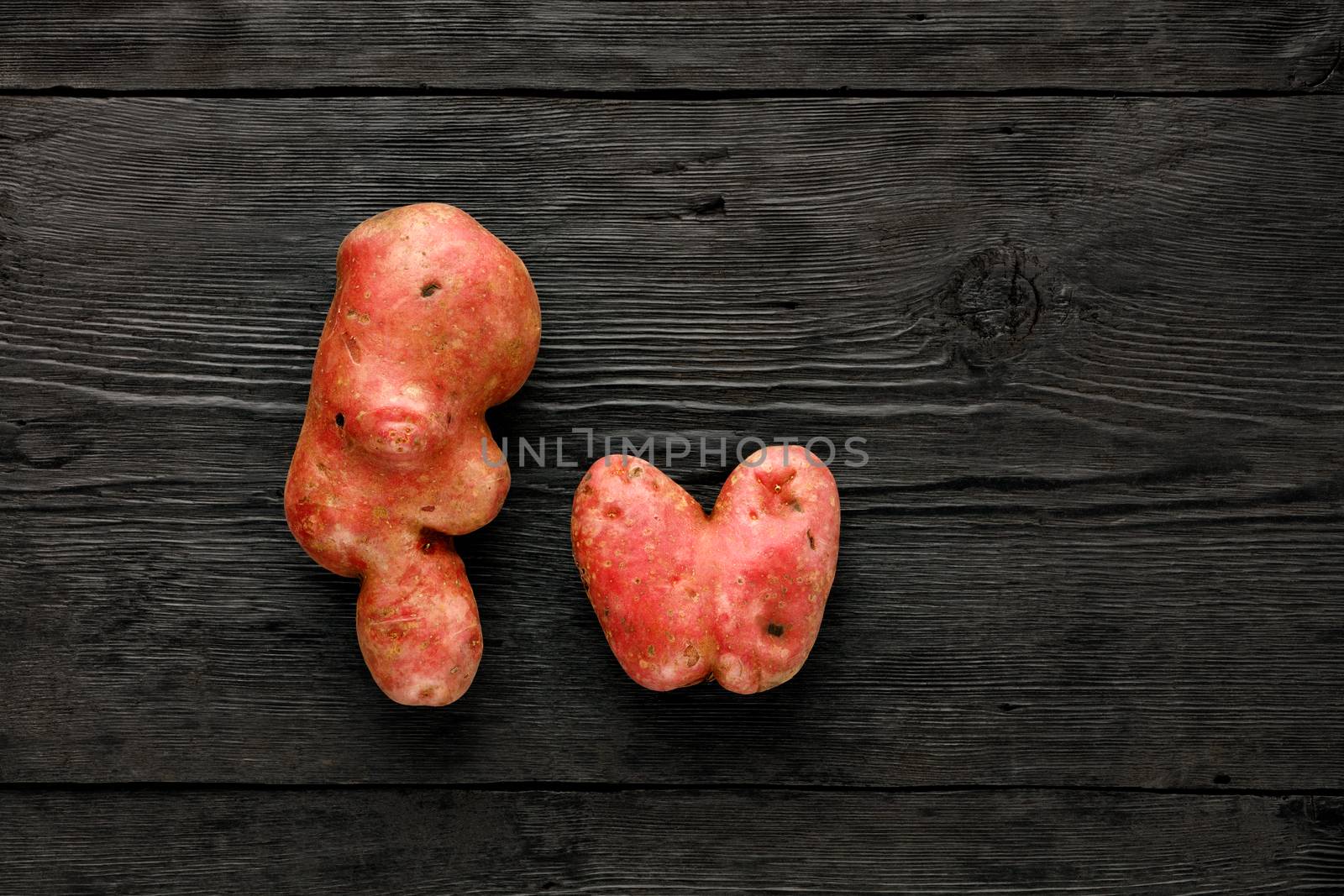 Ugly funny vegetables, heart-shaped potatoes and letter shape on a black wooden background. The concept of grungy vegetables or food waste. Top view, copy space.