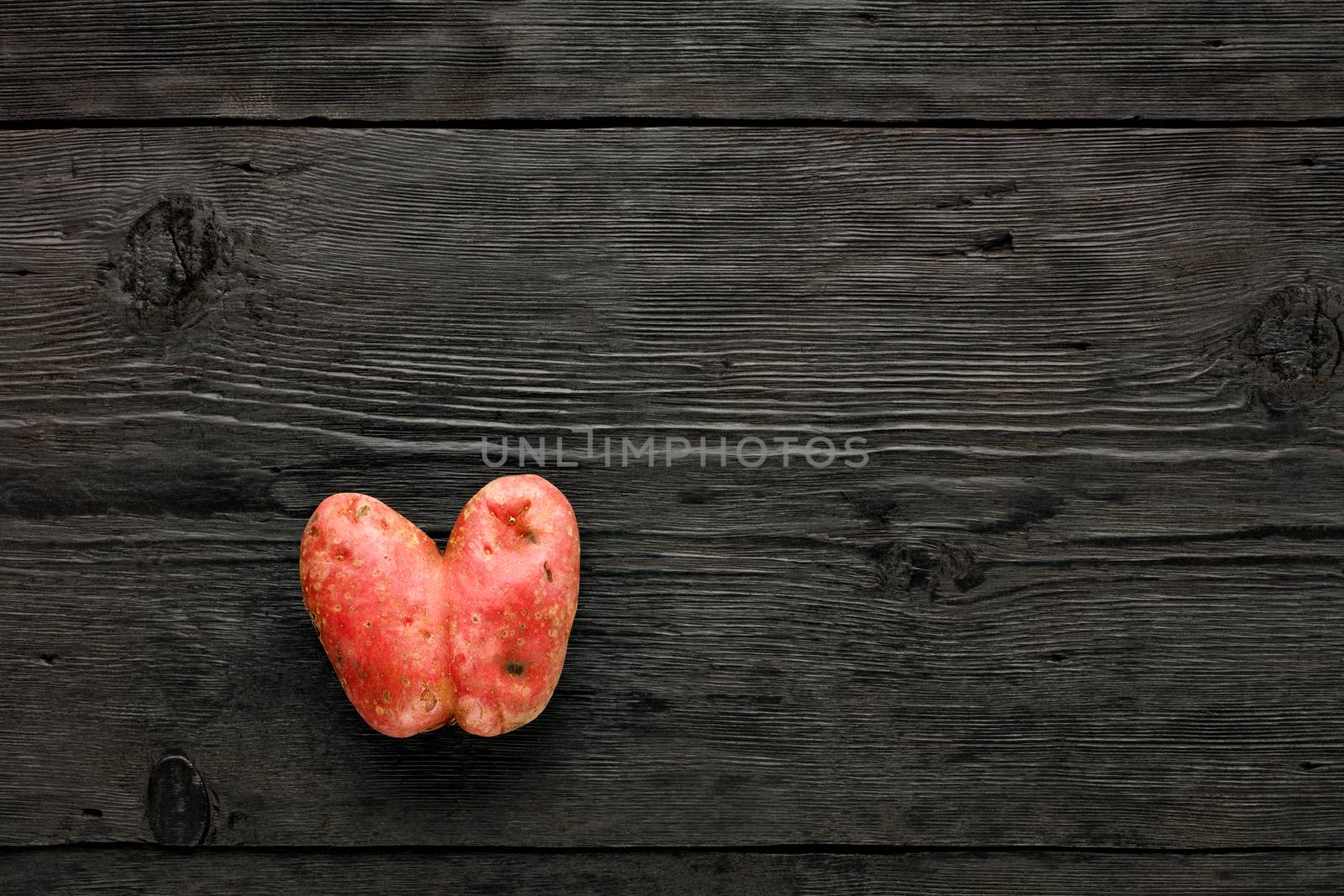 Ugly funny vegetables, heart-shaped potatoes on a black wooden background. The concept of grungy vegetables or food waste. Top view, copy space.