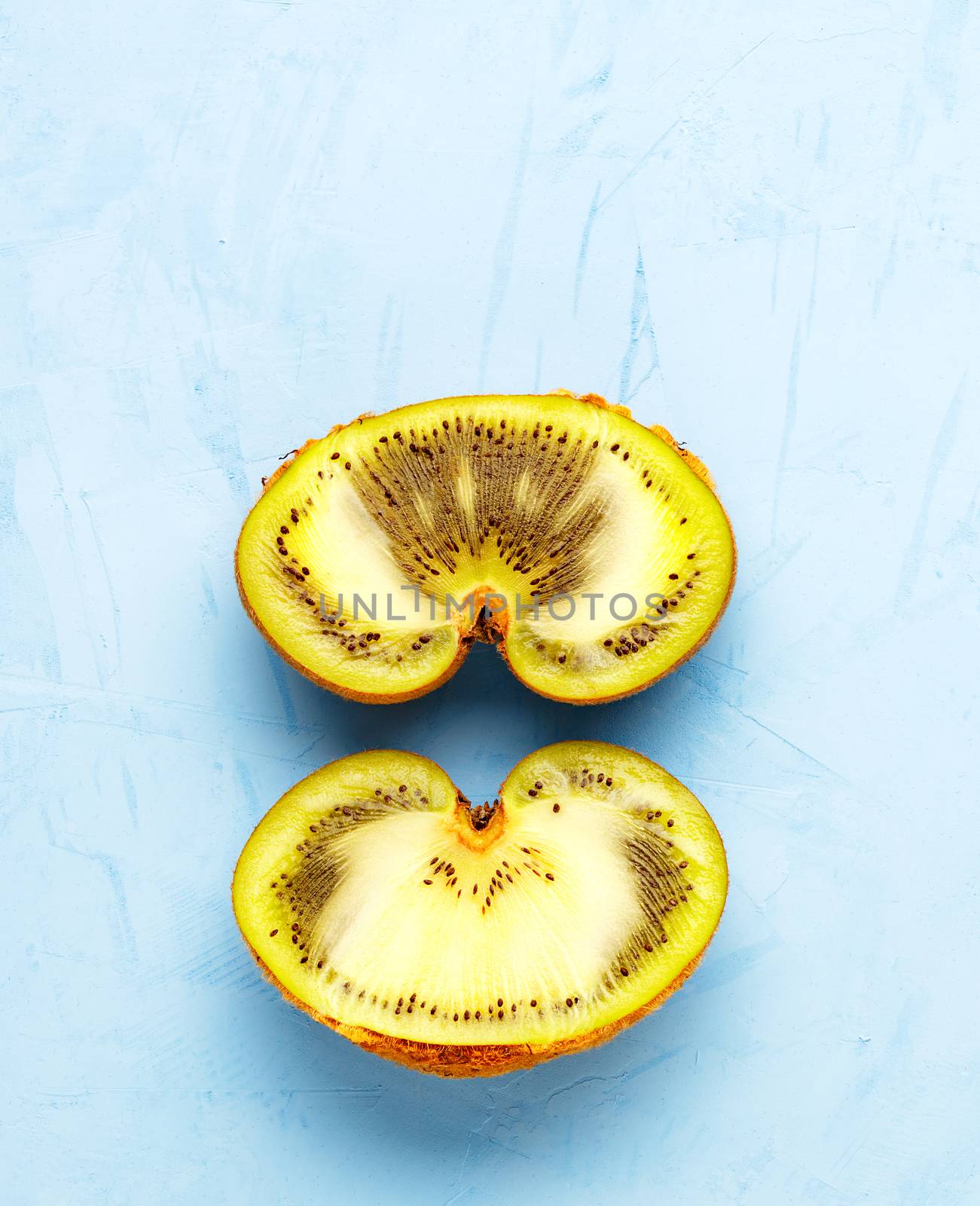 Green ripe kiwi on a blue plaster surface is cut in half, a beautiful pattern of the inner green pulp of the fruit. Top view, horizontal image, copy space.