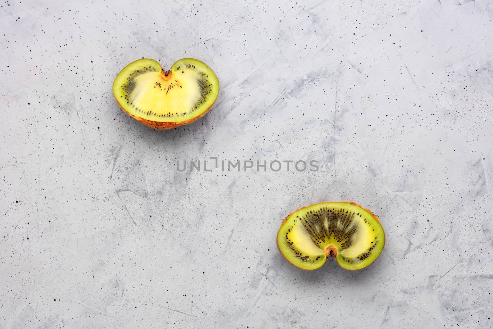Ugly green kiwi on a gray concrete background cut in half, a beautiful pattern of the inner green pulp of the fruit. Top view, copy space.
