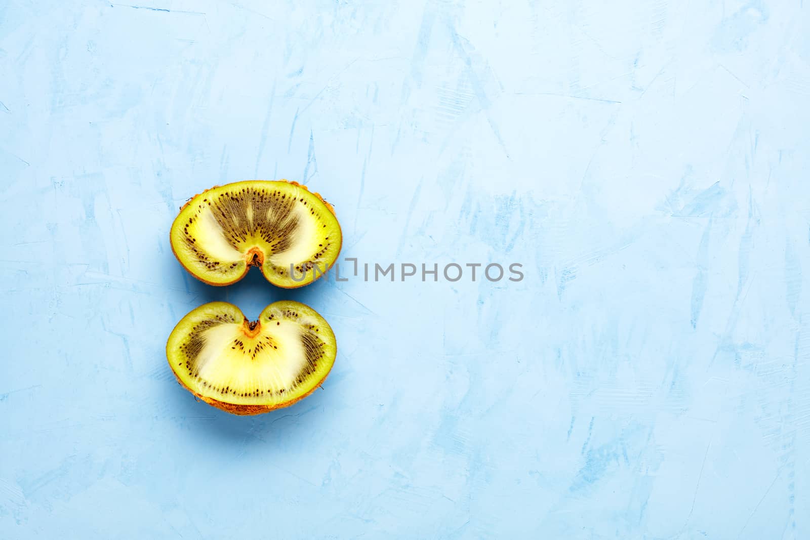 Green ripe kiwi on a blue plaster surface is cut in half, a beautiful pattern of the inner green pulp of the fruit. Top view, copy space.
