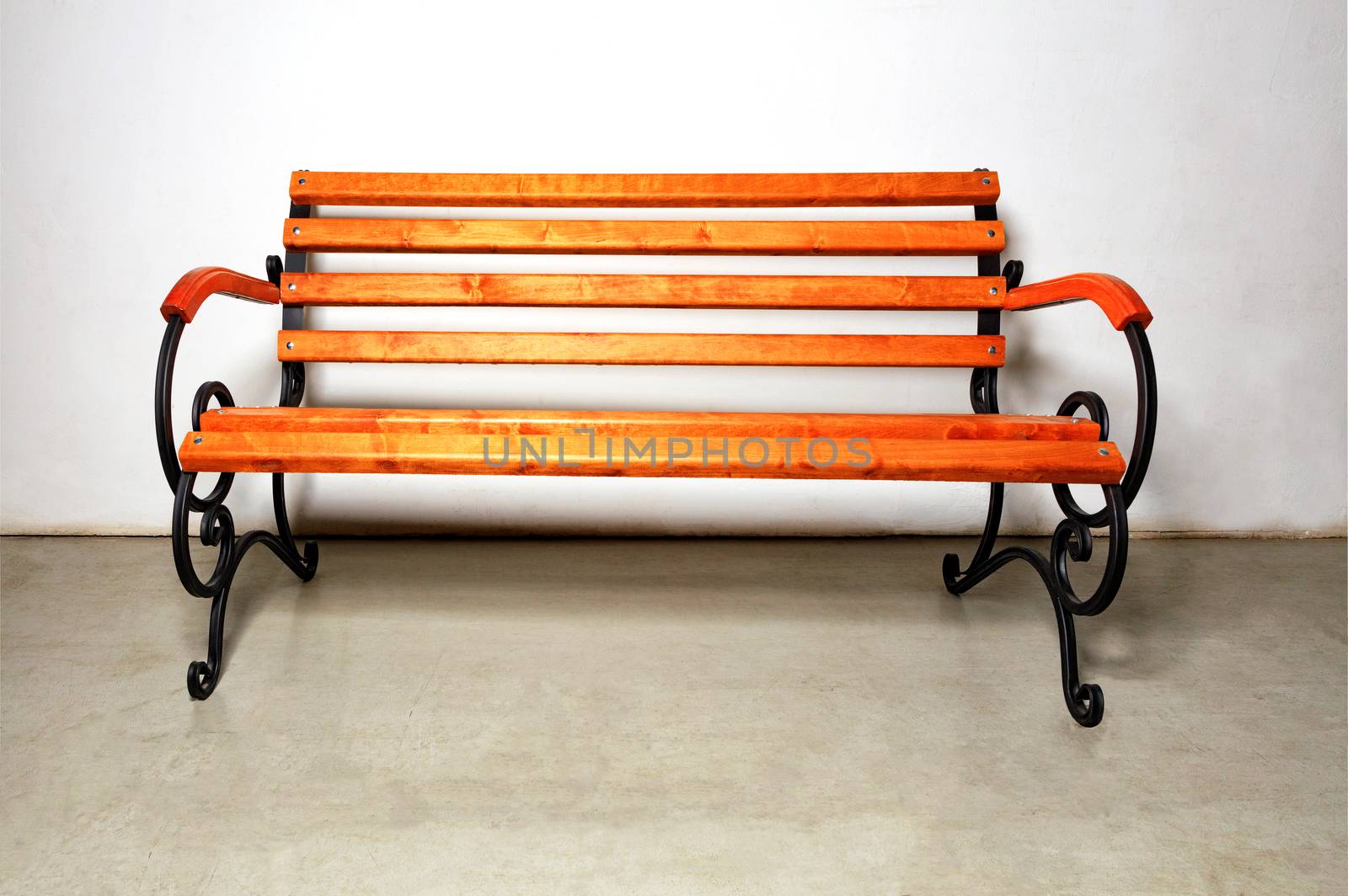 A beautiful wooden bench for rest with a metal forged base for landscaping walking areas in city parks against a white wall of a building and concrete floor, copy space.