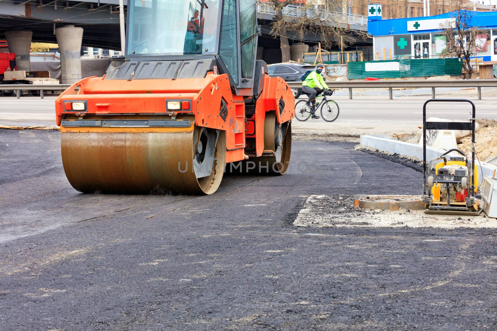 A heavy vibratory roller compacts hot asphalt on the roadway on a clear sunny day. by Sergii