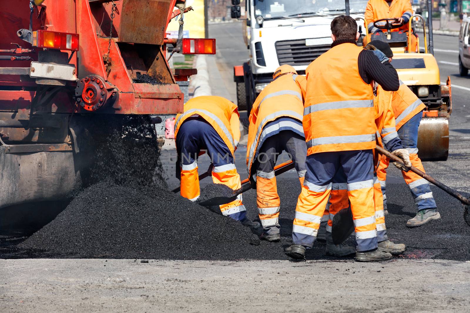 The working team scatters a part of the asphalt with shovels to repair a section of the road. by Sergii