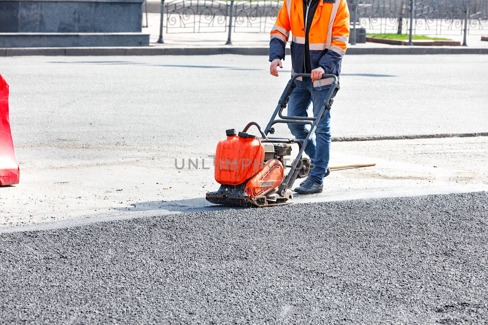 A road worker compacts asphalt with a gasoline vibratory compactor. by Sergii