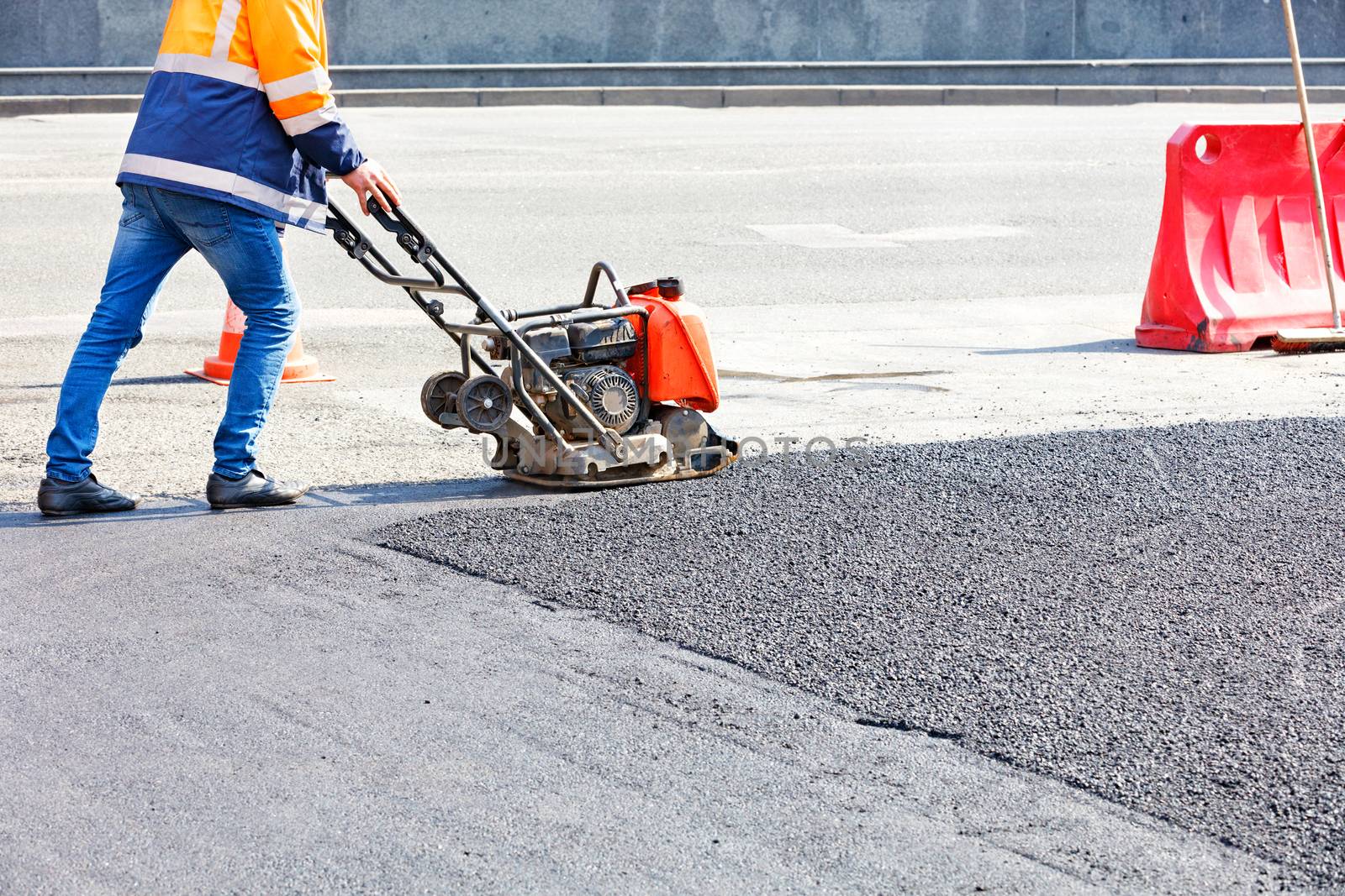 Worker road service use vibratory plate compactor compacting asphalt at road repair site.